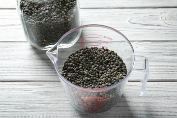 Measuring cup with black lentils on light background