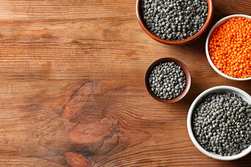 Bowls with red and black lentils on wooden background