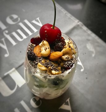 a glass of yogurt, with Cherry, sesame, walnut, dried fruit, kiw and cream
