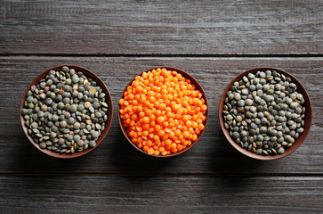 Bowls with red and black lentils on wooden background