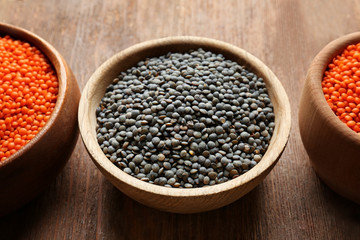 Bowls with red and black lentils on wooden background