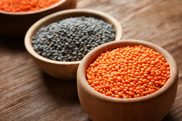Bowls with red and black lentils on wooden background