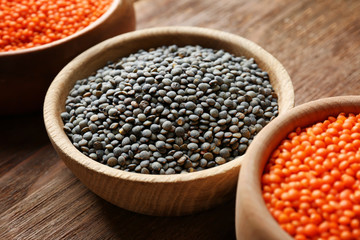 Bowls with red and black lentils on wooden background