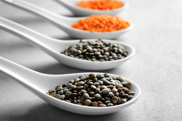 Ceramic spoons with black and red lentils on grey background