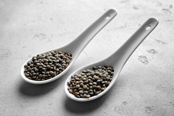Black lentils in ceramic spoons on grey background