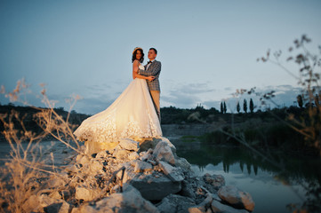 Beautiful wedding couple holding hands and looking at each other in the countryside next to the lake in the evening.