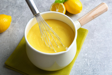 Sauce pan with delicious lemon curd and whisk on table