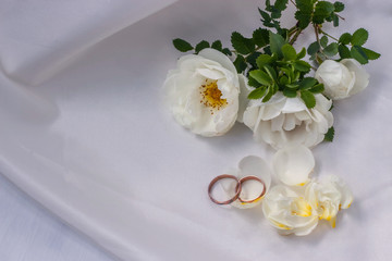 Obraz na płótnie Canvas flowers white wild rose and Golden wedding rings on white pearl color fabric
