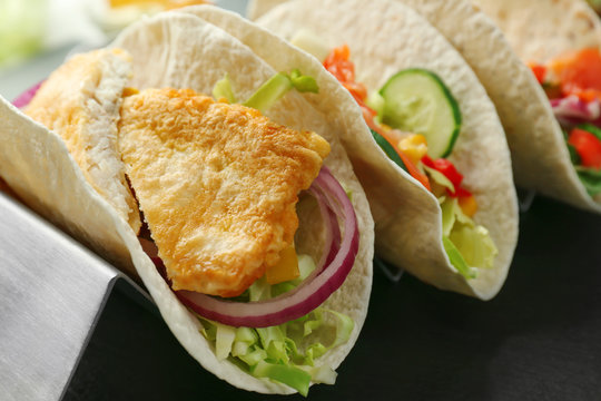 Stand with tasty fish tacos on dark table