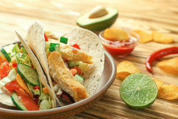 Tasty fish tacos on plate with chips on wooden background