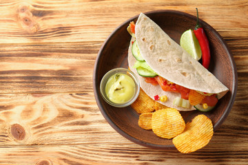 Tasty fish taco on plate with sauce and chips on wooden background