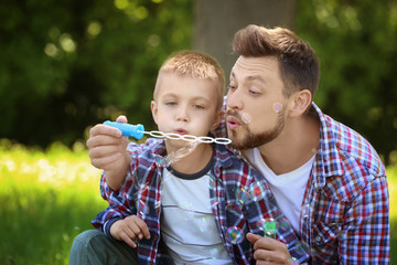 Dad and son blowing bubbles in the park on sunny day