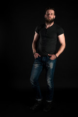 Naklejka premium A charismatic and stylish man with a beard stands full-length on a black isolated background. Vertical frame