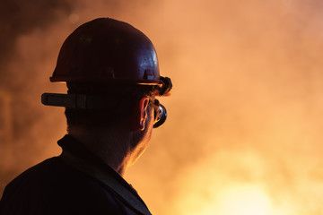 Rear view of foundry worker with a hard hat and safety googles next to a molten metal.Copy space, shallow doff - obrazy, fototapety, plakaty