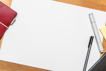 Blank piece of paper on table top, with marker, pen, post-it note, phone and book