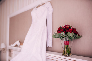 Wedding dress hanging on a wall next to a red bouquet and wedding shoes