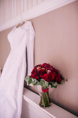 Wedding dress hanging on a wall next to a red bouquet and wedding shoes