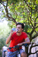 Fototapeta na wymiar young man sit on bike in wood resting drink water