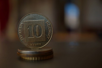 Macro detail of a metal Israeli coin (10 Shekels, ten ILS) on the top of column created of coins with a positive colorful warm background