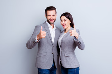 Two smiling happy businesspeople in formalwear showing thumbs-up on gray background