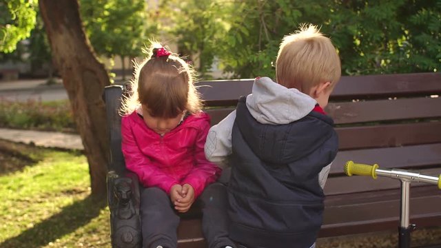 Little cute boy kissing sad little girl on a Park bench.