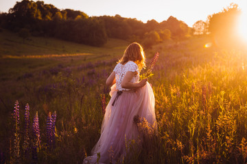 Stunning woman in bright dress walks across the field in the rays of sunset