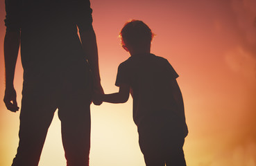 silhouette of father and son holding hands at sunset