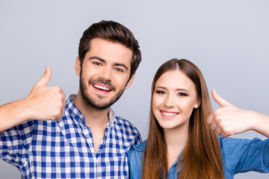 Cheerful brother and sister are gesturing thumbs up at the light background. They are so playful and have beaming smiles, wearing casual outfits, bonding