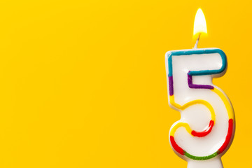 Number 5 birthday celebration candle against a bright yellow background