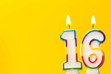 Number 16 birthday celebration candle against a bright yellow background