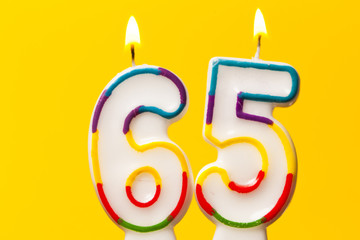 Number 65 birthday celebration candle against a bright yellow background