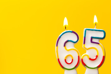 Number 65 birthday celebration candle against a bright yellow background - obrazy, fototapety, plakaty