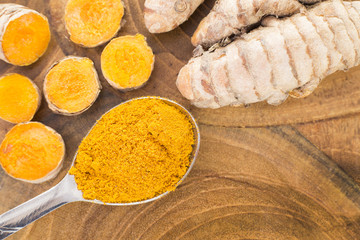 The turmeric powder in spoon and roots on wooden plate - Curcuma longa