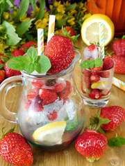 Glass jug is full of ice cubes, berries, lemon and mint is prepared to be filled with a drink on a wooden background