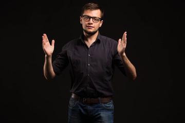 Young glad man portrait of a confident businessman showing by hands on a black background. Ideal for banners, registration forms, presentation, landings, presenting concept.