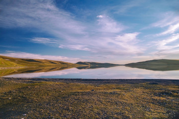 Fototapeta na wymiar The mountain lake in beams of the evening sun. Mongolian Altai. Summer landscape. Lake and mountains against the background of the colorful evening cloudy sky. Nature and travel. Mongolia
