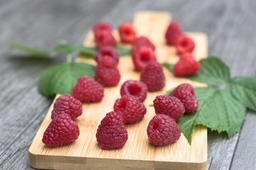 Ripe raspberries on a wooden cutting board and a wooden table.