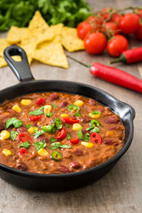 Traditional mexican tex mex chili con carne in a frying pan on wooden table
