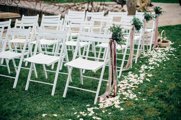 decorated outdoor wedding ceremony white wooden chairs and flowers