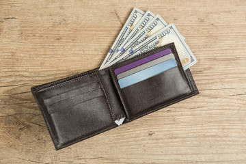 Wallet with 100 dollar bills on a wooden table