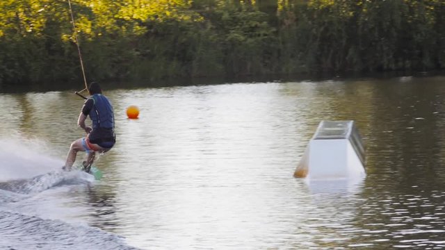 Wakeboarder ride on cable wakeboard in park, outdoor extreme slow motion on water, surfing athlete on water doing boardslide, noseslide or tailslide 180 out, backside bluntslide