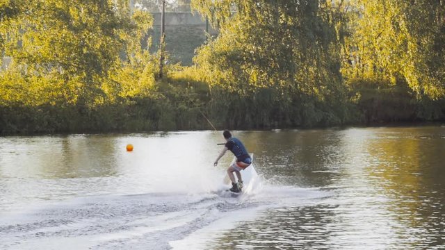 Wakeboarder ride on cable wakeboard in park, outdoor extreme slow motion on water, surfing athlete on water doing boardslide, noseslide or tailslide 180 out, backside bluntslide