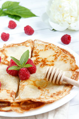 Thin pancakes with honey and raspberries on a white plate