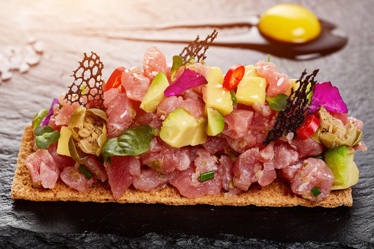 fresh tuna tartar with salt and herbs, studio shot. Fish tartar on black shale.