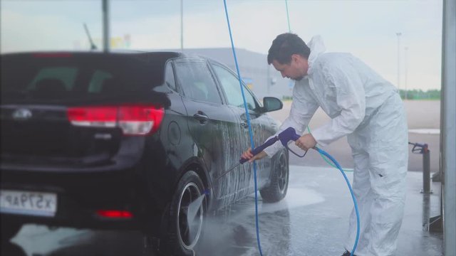 Young caucasian man washing his car using water spray on the car wash self-service. Car washing with water. Water spray machine.