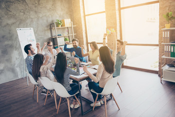 We are the champions! Successful business team with raised up hands in light modern workstation, celebrating the breakthrough in their company