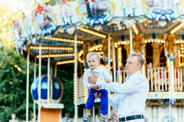 Happy father throwing his son high in front of carousel in amusement park