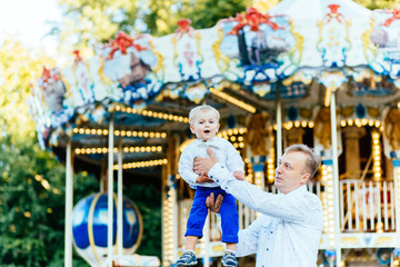 Obraz na płótnie Canvas Happy father throwing his son high in front of carousel in amusement park