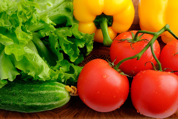 Branch of fresh red tomatoes, yellow bell pepper, green cucumbers and lettuce on a wooden cutting board
