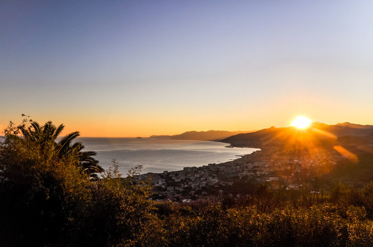 Stunning ligurian coastline at sunset as seen from Borgio Verezzi - Liguria, Italy. Evening scene shortly before sunset with the ocean, mountains in the background and a palm tree in the foreground.